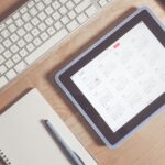 A tidy desk setup featuring a tablet displaying a calendar, keyboard, and stationary items.
